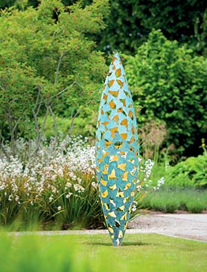 Quill sculpture poised on a lawn with flowers behind