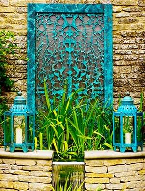 Filigree water wall with verdigris bronze patterned surface backed by reflective stainless steel