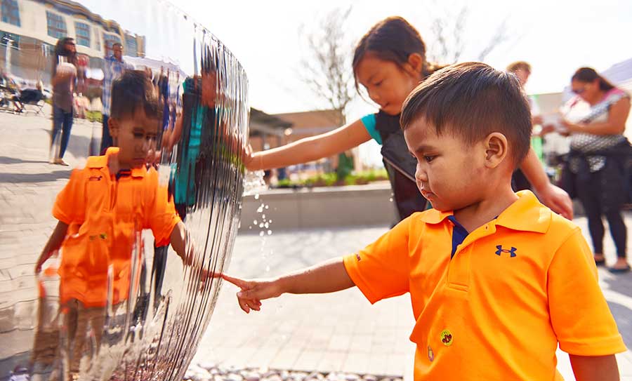 Niños interactuando con la fuente ornamental Cáliz en una plaza pública del Liberty Centre