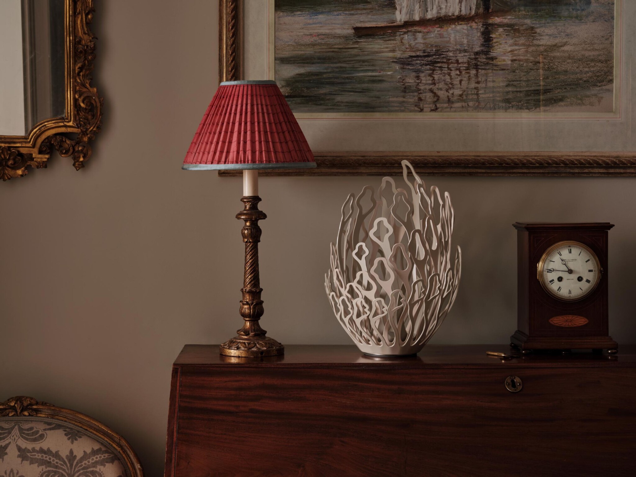 Table with a red lampshade, white decorative bowl, vintage clock, and tips on how to display sculptures at home.