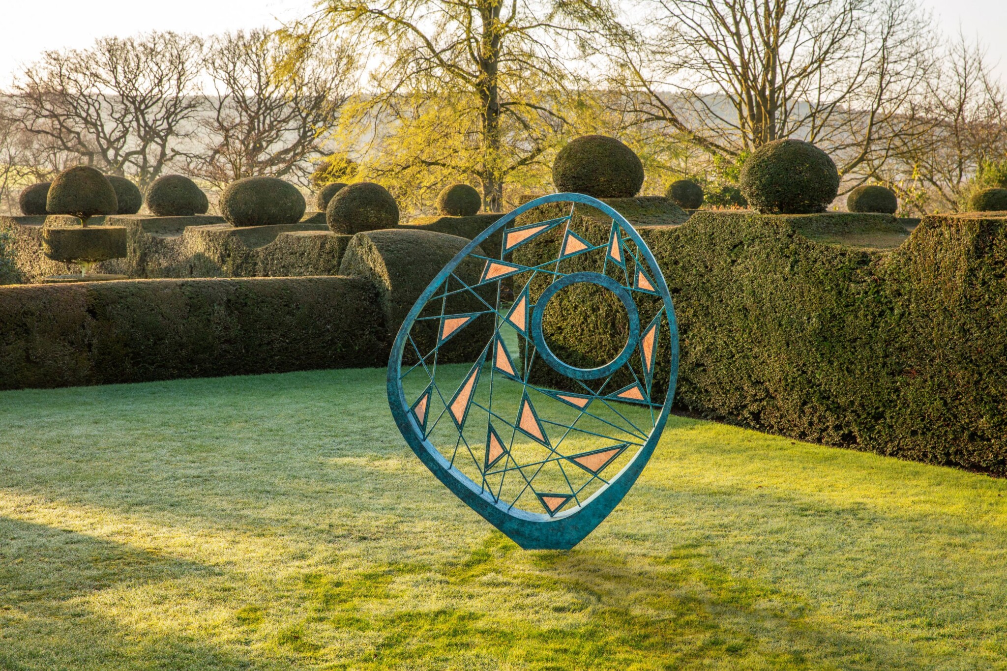 Large bronze sculpture in a formal style topiary garden.