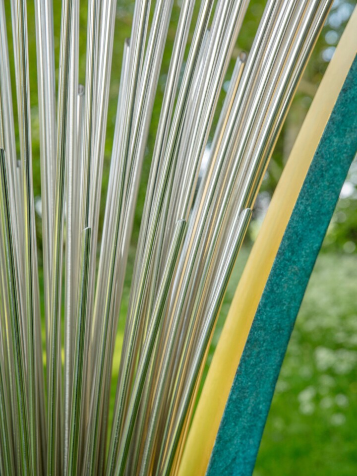 Close-up of stainless steel rods beside a teal and yellow surface, part of a contemporary abstract sculpture.