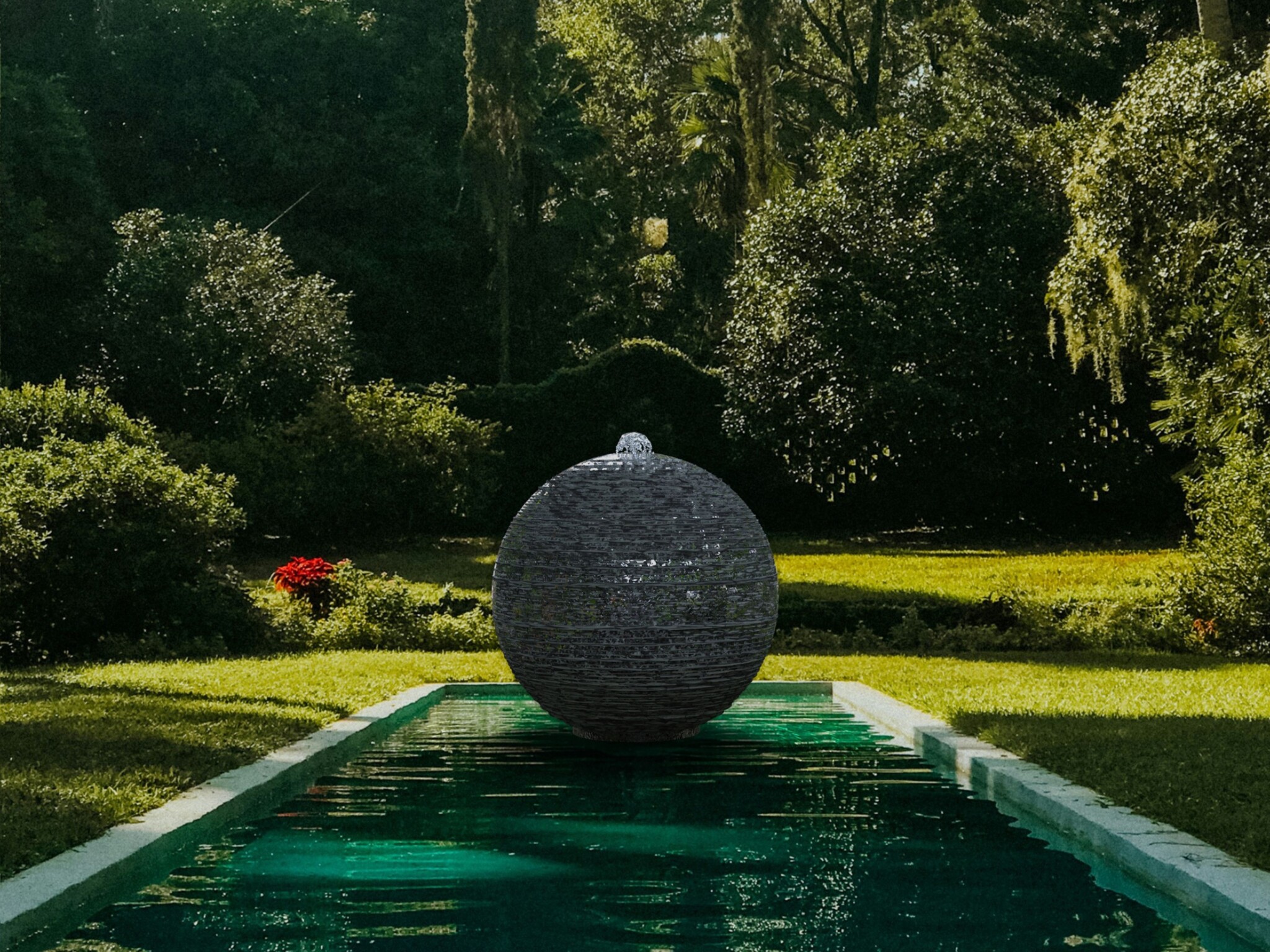 Stone sphere water feature made with layers of Welsh slate with a bubbling fountain, placed on a pool of water surrounded by woodland.