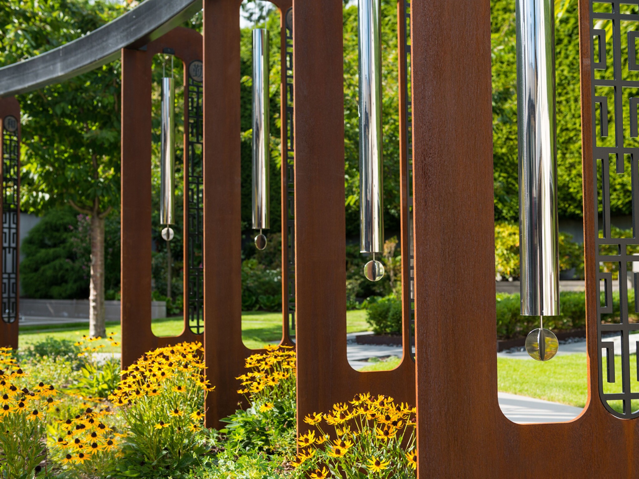 Snapshot of a giant windchime sculpture made up of corten steel panels and stainless steel tubes.