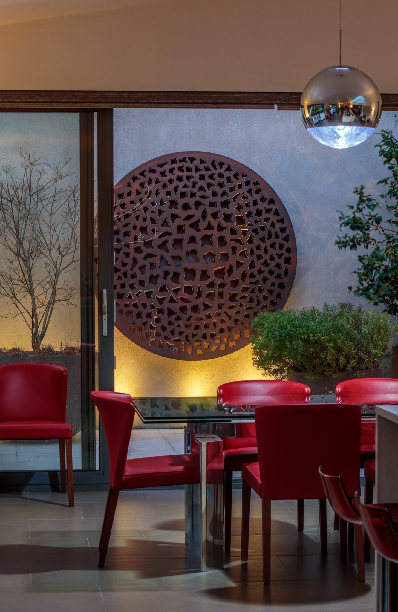 Modern dining area with red chairs, glass table, illuminated art for lounge, and a large decorative panel outside.
