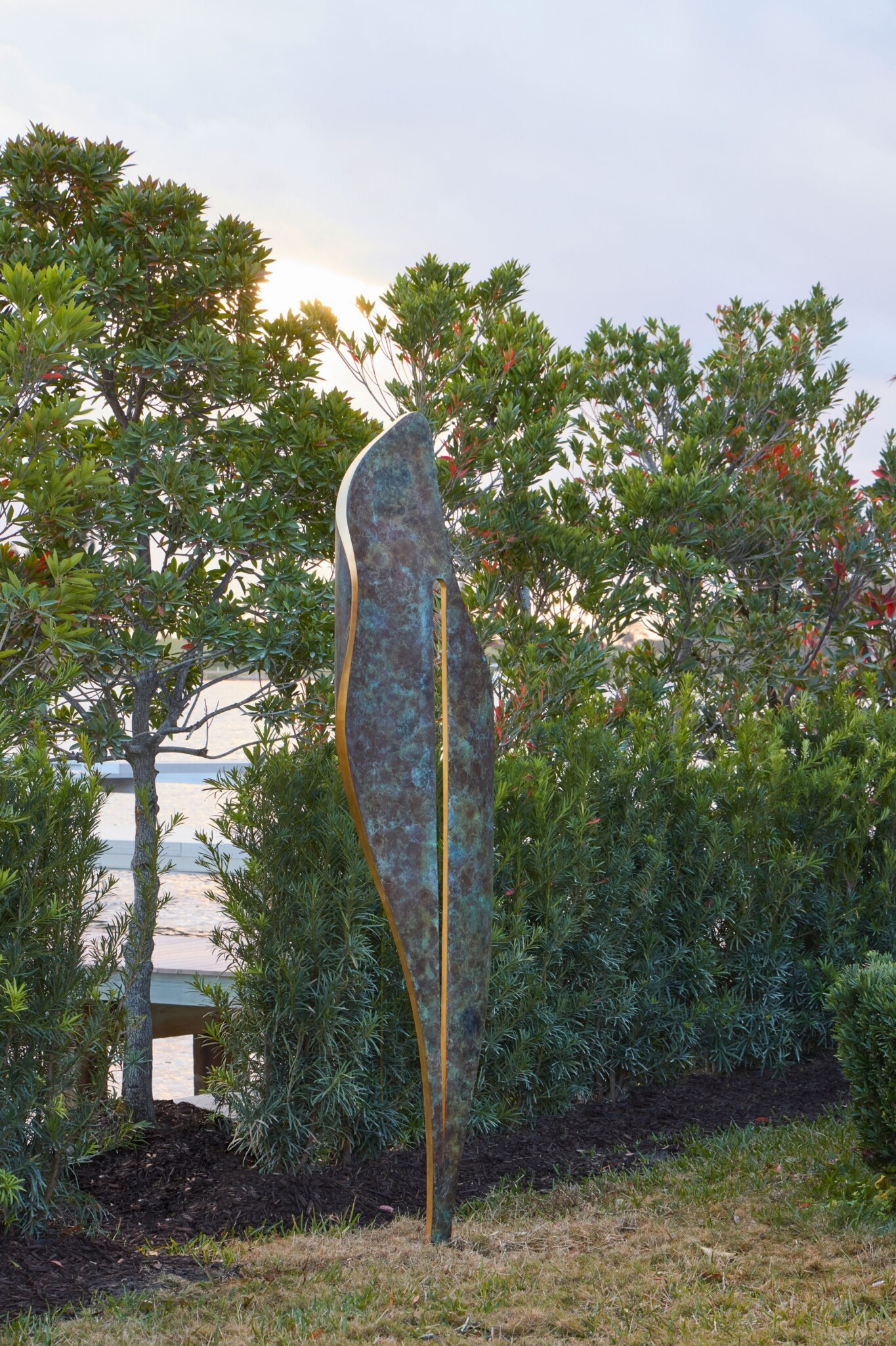 Bronze leaf-like sculpture in a coastal garden setting.