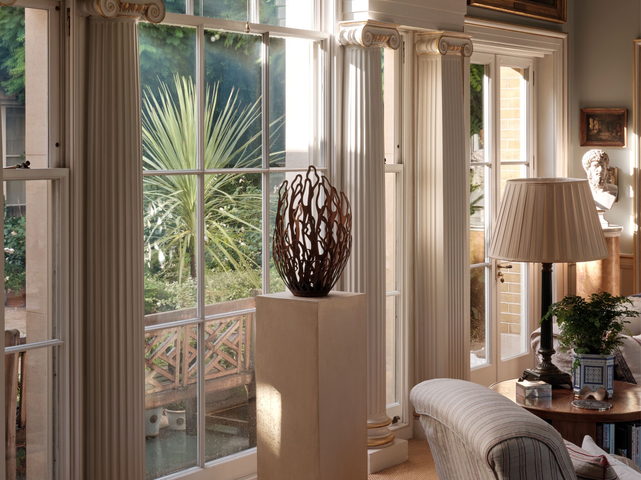 Sunlit living room with tall windows, columns, and a modern sculpture—perfect to display sculptures at home.