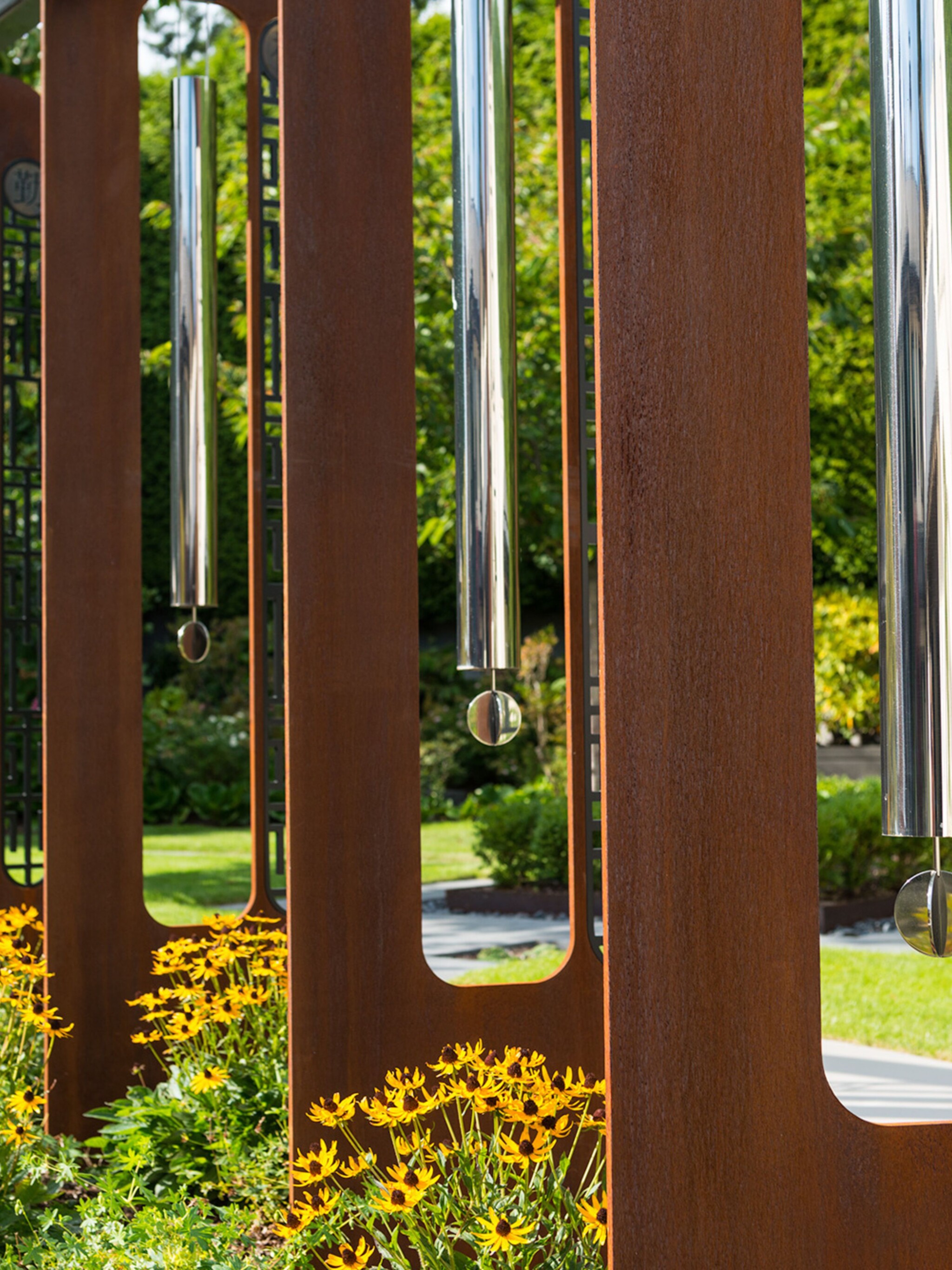 Tubes of stainless steel hang between blades of Corten steel to make a giant outdoor sculpture in the likeness of wind chimes