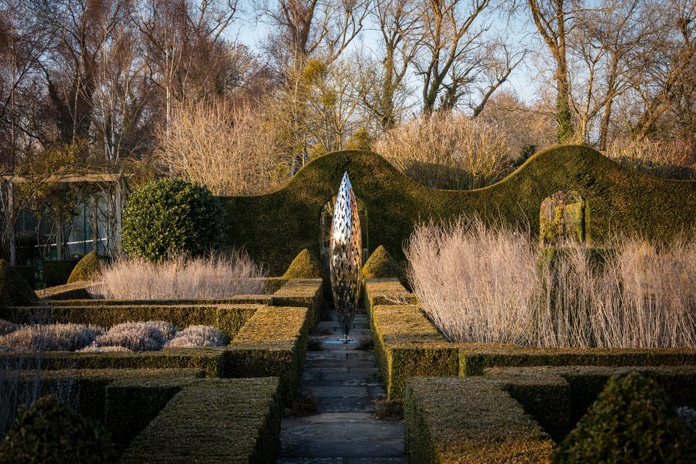 formal garden path with a narrow central water rill flanked by clipped hedges and framed by background trees