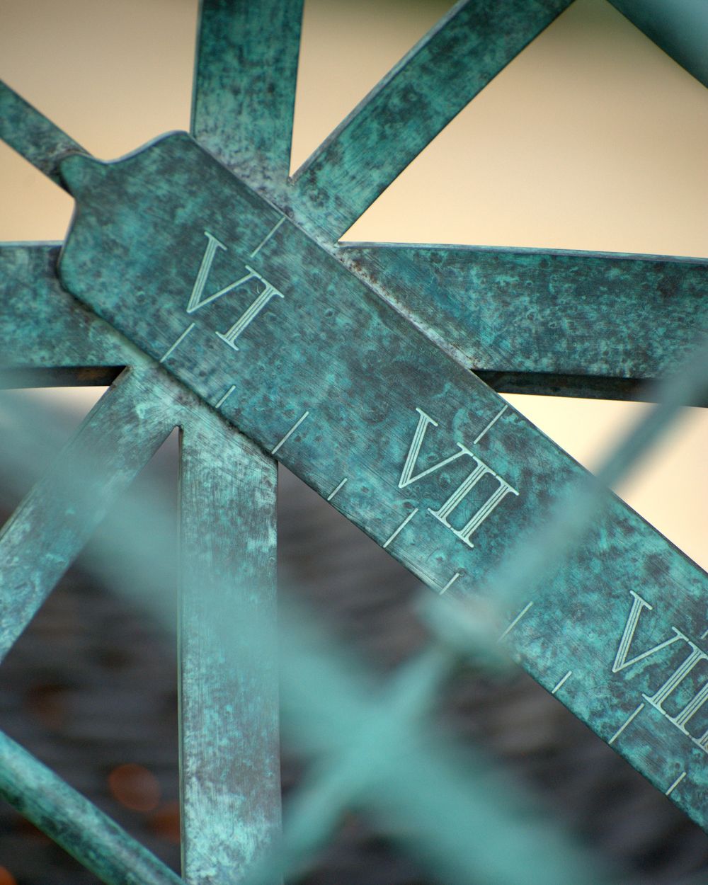 Close-up of a weathered sundial with Roman numerals VI, VII, and VIII engraved on a greenish metal surface.