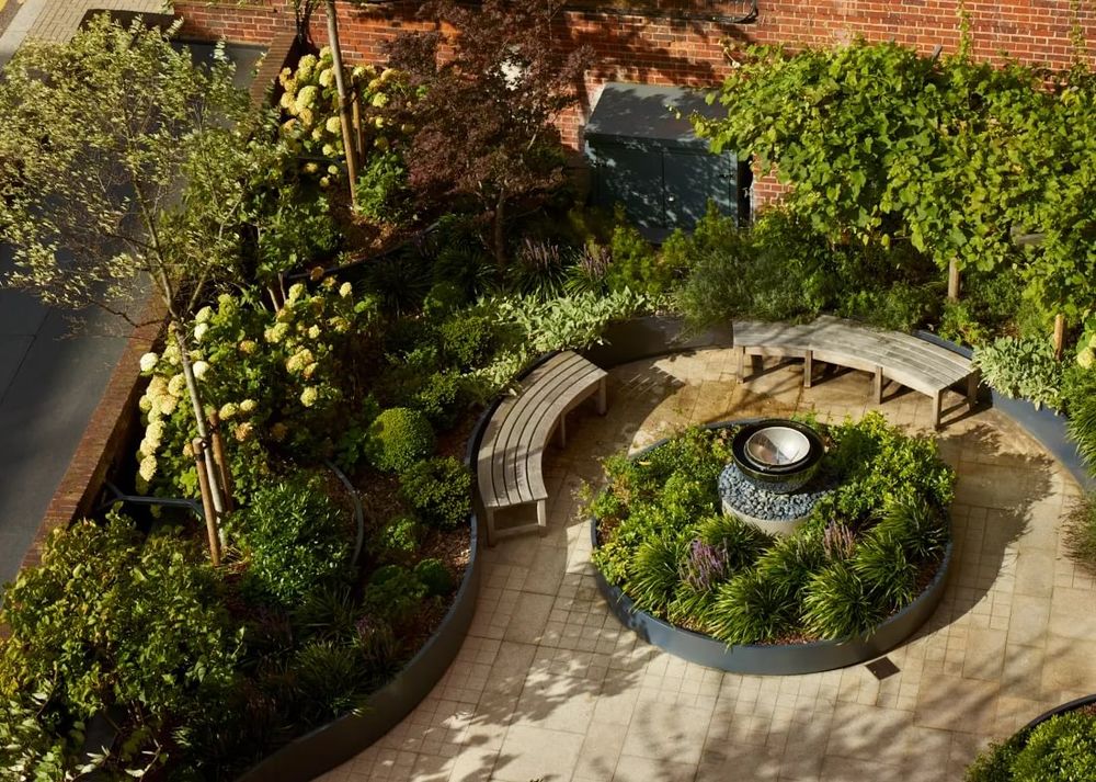 Curved benches surround a circular garden with lush plants and a fountain, showcasing architectural garden design.