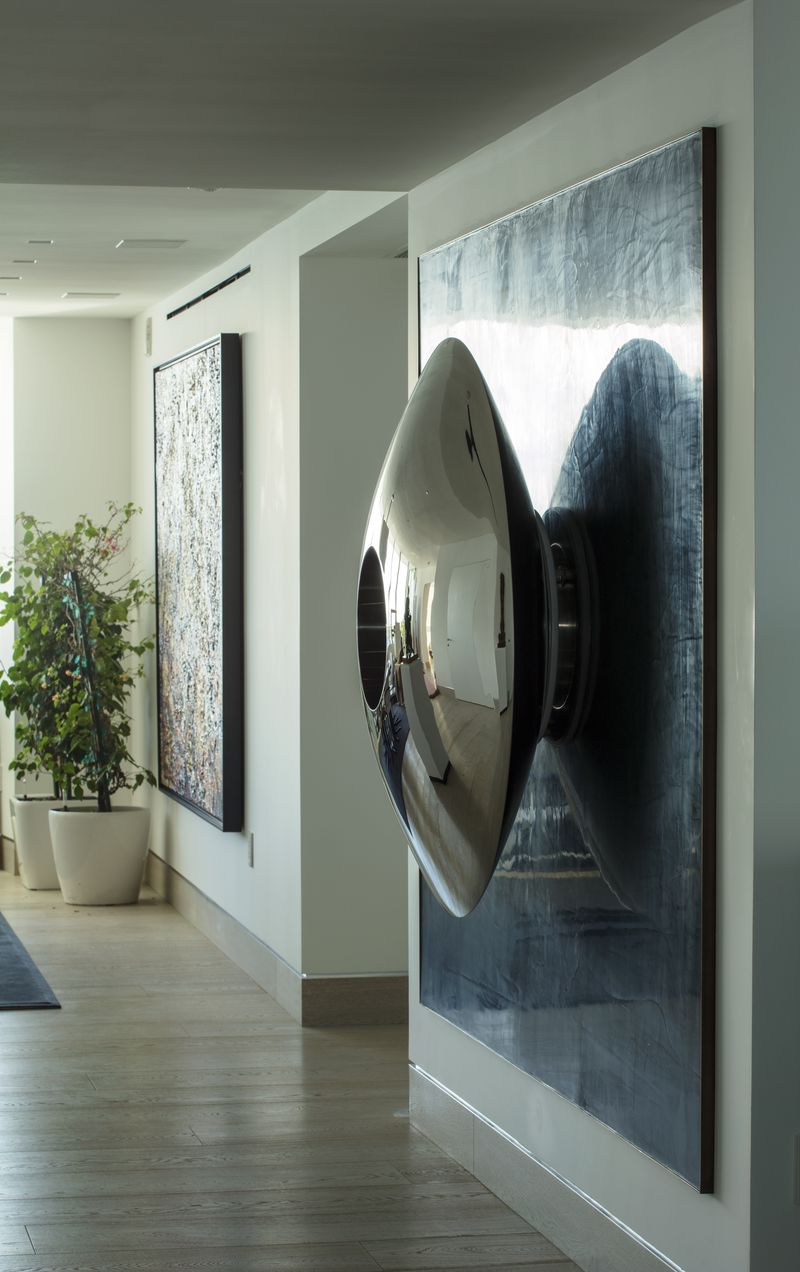 A shiny, metallic, cone-shaped sculpture is mounted on a wall—perfect for hallway sculpture ideas in modern spaces.