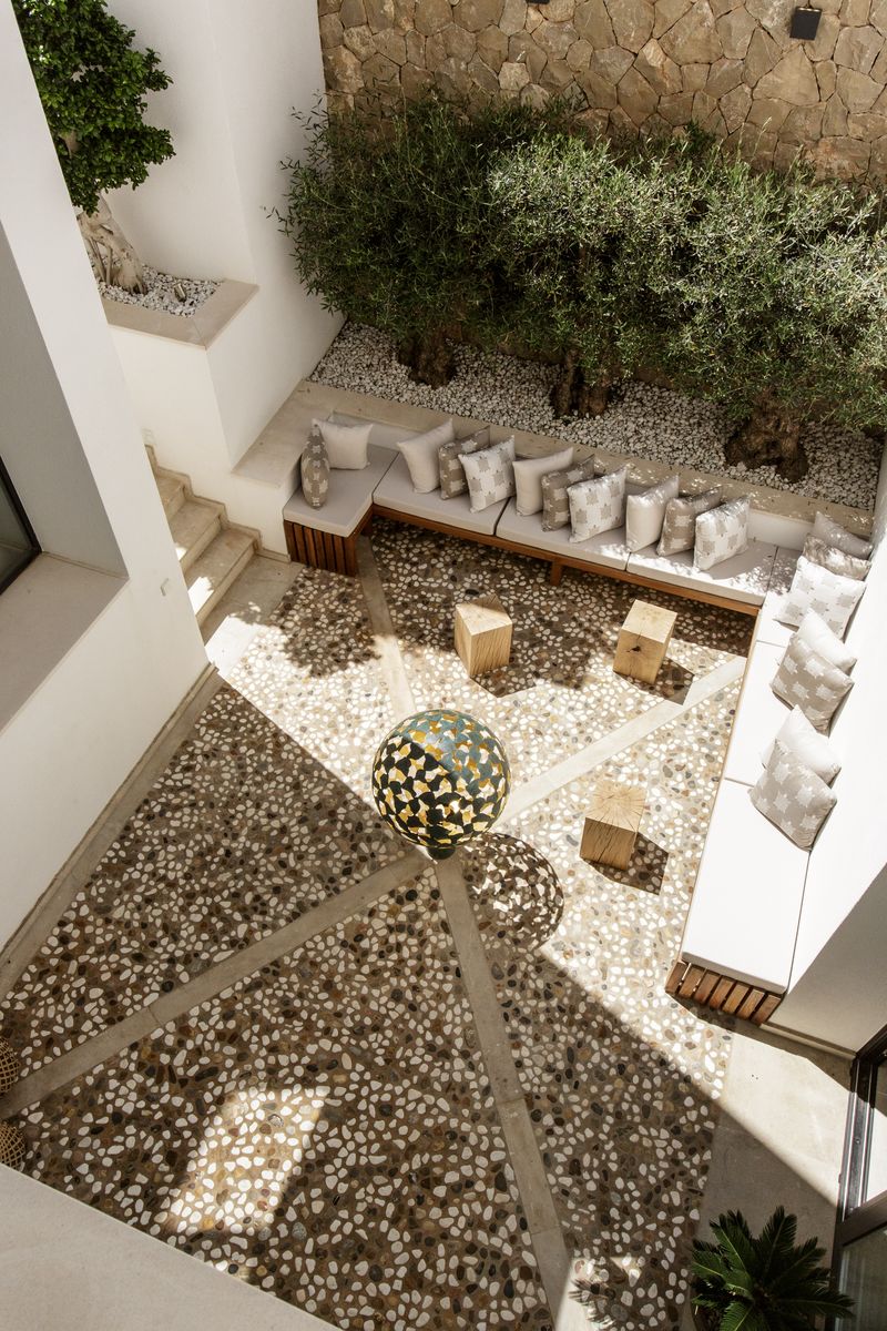 Stone courtyard with built-in seating, white cushions, pebble floor—perfect for unique courtyard garden ideas and relaxation.