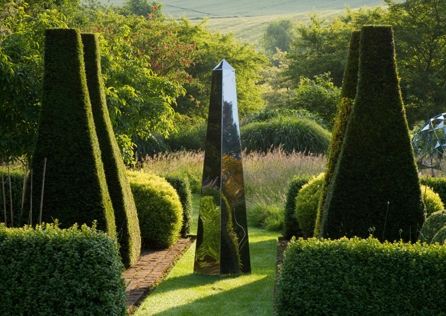 A shiny black obelisk stands in a manicured garden, offering inspiration for unique garden sundial ideas.