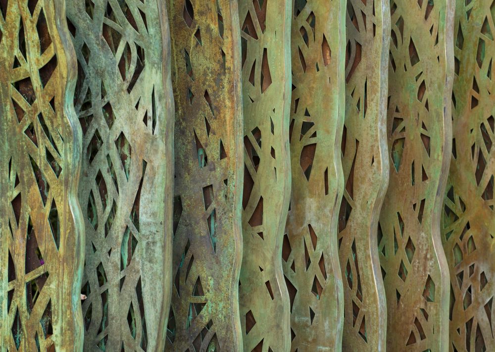 artwork featuring massive vertical panels crafted with organic, custom-perforated openwork patinas, designed to mimic intricate natural lattices