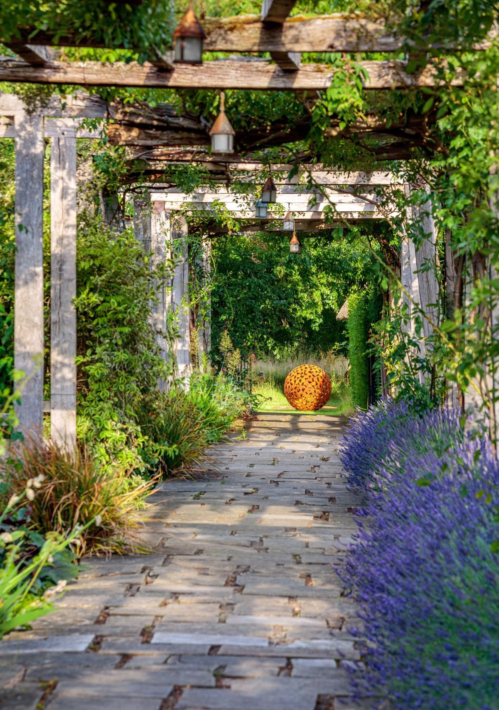stone path under a wooden pergola leading to corten steel sculpture
